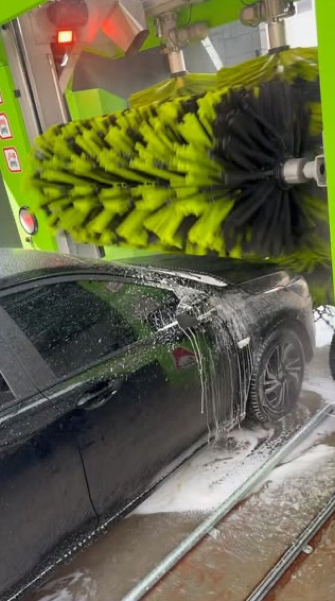 Escova da máquina do Whasher passando sobre um carro preto coberto de espuma